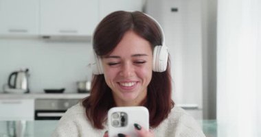 Çekici esmer kadın beyaz koltukta otururken görüntülü sohbet eden biriyle konuşuyor..