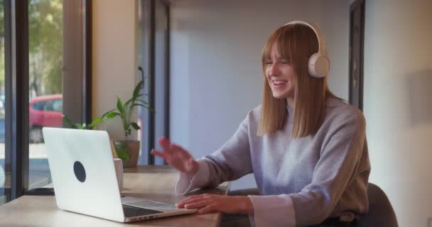 Młoda blondynka wint słuchawki za pomocą komputera podczas konferencji cal siedzi w kawiarni — Wideo stockowe