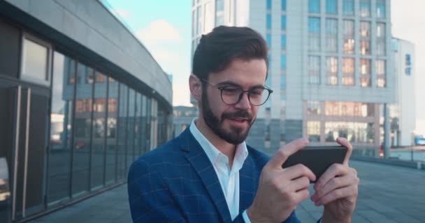 Aantrekkelijke casual zakenman spelen op smartphone in het spel en verliezen in stedelijke achtergrond. — Stockvideo