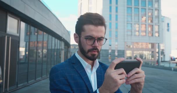 Takım elbiseli adam oyunda akıllı telefonda oynuyor ve şehir arka planında kaybediyor.. — Stok video