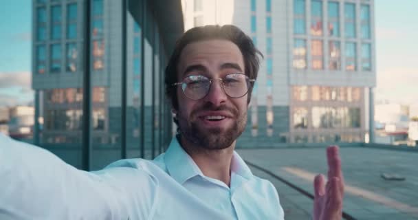 Shot of businessman with glasses making video call standing outdoors in city. — Stockvideo