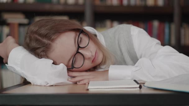 Schoolgirl with glasses learns lessons, cute girl sleeping in library while doing homework. Female tired of extra classes and tutoring. — Stockvideo