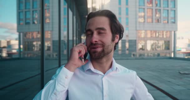 Closeup smiling man talking mobile phone near skyscrapers. Close up of cheerful businessman having phone call. Portrait of happy business man calling phone in outdoor. — Vídeo de Stock