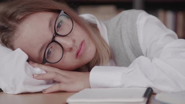 Colegiala con gafas aprende lecciones, linda chica durmiendo en la biblioteca mientras hace la tarea — Vídeos de Stock