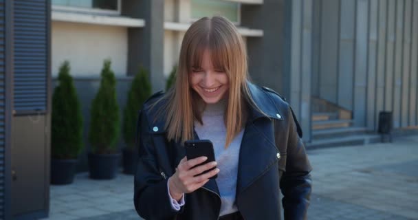 Sorprendido joven rubia mirando en el teléfono inteligente y sorprendido, diciendo WOW. — Vídeo de stock