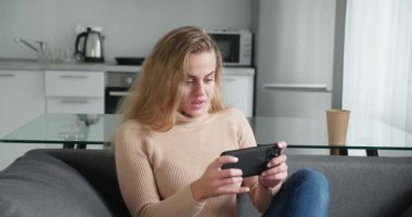 Modern mutfak arka planında akıllı telefonları olan bej renkli yün kazaklı sarışın bir kadın..