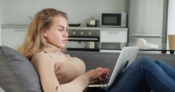深刻なかなり若い女性フリーランスは、ラップトップに焦点を当てた女の子の研究のためのコンピュータを使用して、現代の家庭タイプの電子メールからのフリーランスで動作しますオンラインソファの上に座っている女性ユーザー忙しいです距離インターネットの仕事 — ストック動画