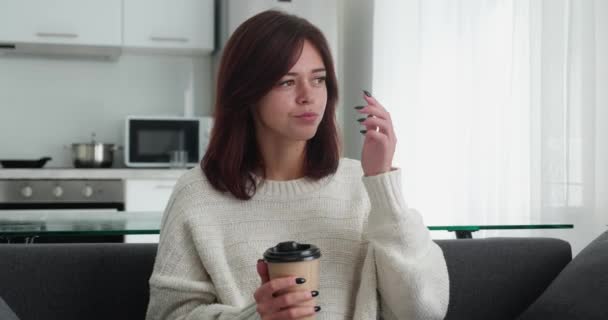 Satisfied young lady in cozy sweater relaxing with hot mug of tea on couch. Beautiful female enjoy weekend at home having positive emotion — Vídeo de Stock