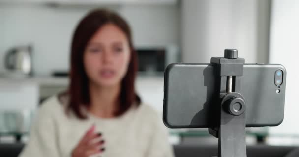 여성 블로거는 거실에서 홀로 소파에 앉아 찍고 있는 스마트 폰을 이용해 비디오를 녹화 한다. 삼각대로 전화에 집중하 세요.. — 비디오