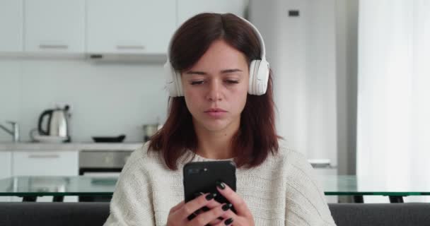 Millennial girl in headphone smiling and feeling happy to get good news from smartphone — Stockvideo
