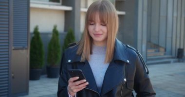 Heyecanlı sarışın genç bayan kazanan akıllı telefona bakıyor dışarıda ayakta durarak online başarısını kutluyor. Öforik kadın yeni bir iş fırsatı yakaladı, e-postada iyi haberler okuyor, zafere seviniyor,