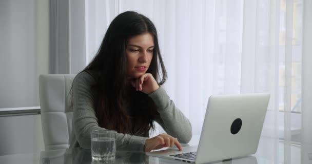 Femme brune aux cheveux longs ont chat vidéo dans son ordinateur portable assis de fond intérieur de la cuisine. Femme sourit en agitant la main tout en regardant l'écran. Concept enseignement à distance. — Video