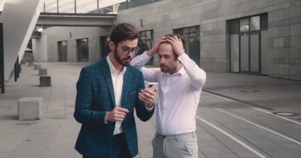 Двое бизнесменов читают хорошие новости на своих смартфонах и счастливо танцуют. Удачи на свежем воздухе. — стоковое видео