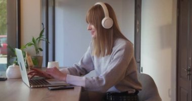 Kulaklıklı çekici sarışın kadın kahve dükkanında oturuyor ve dizüstü bilgisayarla çalışıyor. Serbest çalışan mutlu bir kadın ya da internete girip arkadaşlarıyla sohbet eden biri..