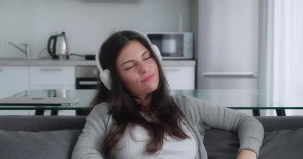 Teen girl listening music sitting in sofa kitchen background — Stock Video