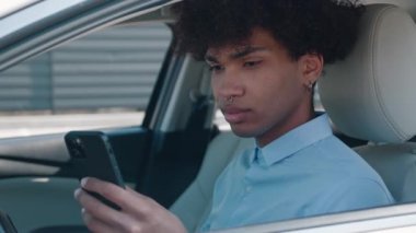 Adam modern bir arabada oturuyor ve akıllı telefon ve kamerayla çalışıyor.