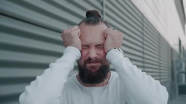 Depresyonda genç bir adam, yakışıklı üzgün bir adam, ofis binasının yanında durmuş kameraya bakıyor, umutsuz, hayal kırıklığına uğramış, başını yana doğru sallıyor ve aşağıya bakıyor.