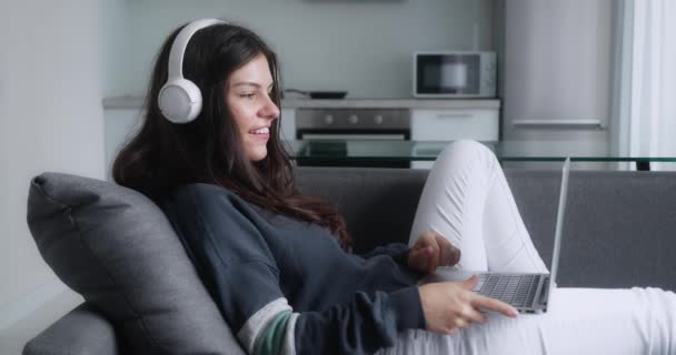 Sonriente señora casual charlando con amigos, trabajando o estudiando desde casa en línea en la tecnología informática relajante en el sofá. — Vídeos de Stock