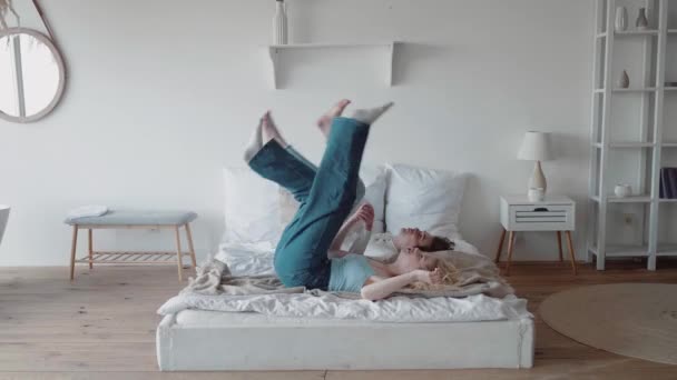 Junges Paar Teenager kommen im Motel an, Kerl springt auf Bett und junge blonde Frau fällt neben ihm — Stockvideo