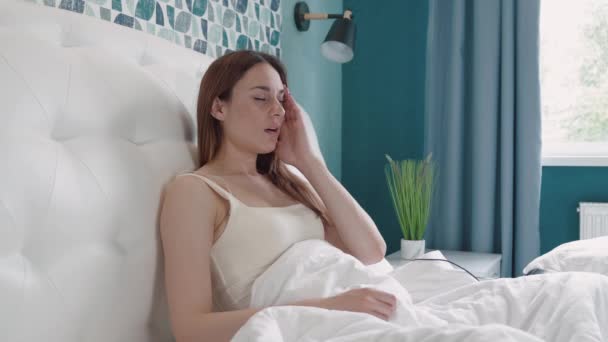 Smutna, przygnębiona, zmęczona młoda kobieta siedząca na łóżku, trzymająca głowę, cierpiąca na migrenę — Wideo stockowe
