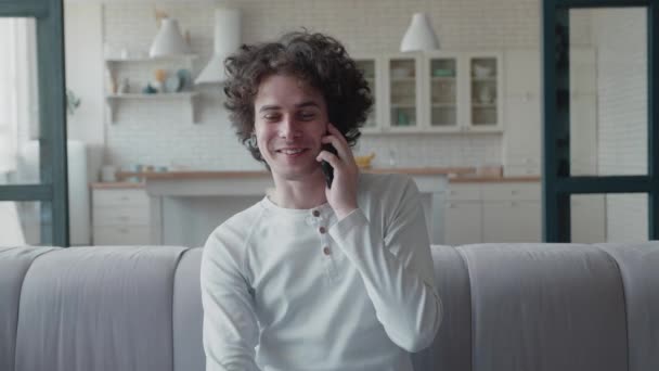 Lockiger Teenager mit Nasenpiercing und Tunneln in den Ohren, der auf dem heimischen Sofa mit dem Smartphone spricht. — Stockvideo