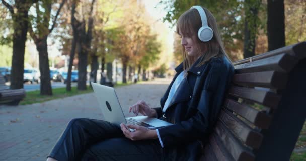 Mladá roztomilá dívka sedí na ulici a píše na klávesnici notebooku. Práce na volné noze odkudkoliv. Komunikace prostřednictvím nejmodernějších technologií. — Stock video