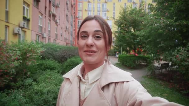 Χαμογελώντας ευχάριστη γυναίκα κάνει χειρονομία γεια, κρατώντας κάμερα στο χέρι της, κλήση συνομιλία, επικοινωνία με συναδέλφους ή freands. Όμορφη γυναίκα blogger καταγραφή βίντεο πάνω από την πόλη bacground — Αρχείο Βίντεο