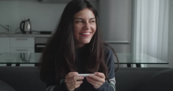 Захоплена молода жінка, що сидить на ліжку вдома, виглядає щасливою після позитивного результату з домашнього тесту на вагітність — стокове відео