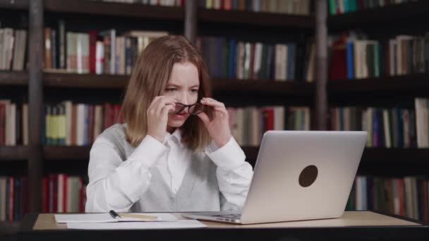 Escolar impactada mirando la pantalla del portátil, se quita las gafas en sorpresa vio noticias inesperadas, sorprendido y sorprendido mirando monitor con la boca abierta en la biblioteca — Vídeo de stock