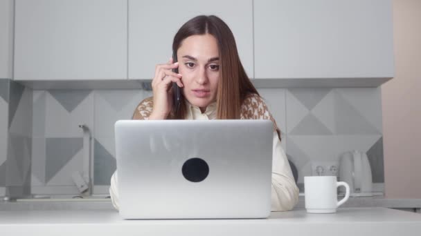 Jonge zakenvrouw met mobiele telefoon tijdens het werken op de computer thuis, vrouwelijke biracial freelancer het maken van online bestelling of communiceren met de klant op afstand en het drinken van koffie — Stockvideo