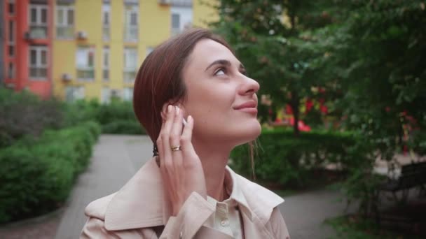 Junge Geschäftsfrau mit drahtlosen Kopfhörern hört Musik in der Stadt über bunten Häusern Hintergrund — Stockvideo