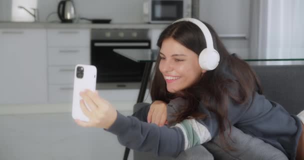 Krásná usměvavá brunetka žena mluví s někým s video chatem, zatímco sedí v útulné pohovce doma — Stock video