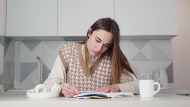 Närbild skott Ung vuxen kvinna läser en bok i köket. Kvinna studerar historia Slappna av hemma. Lärande, kunskap, utbildning, avslappning i vardagen — Stockvideo