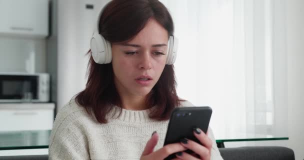 Szomorú nő fejhallgatóval olvasás rossz hír az okostelefon — Stock videók