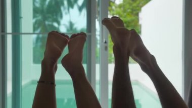 Tatildeki genç bir çiftin bacaklarının silueti. Panoramik pencerelerin ve ormanın zemininde yatıyorlar.