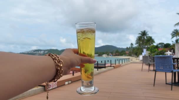 Tenant main grand verre classique de bière contre une mer bleu turquoise. Condenser sur un verre avec de la bière. Vacances d'été détendues au bord de la mer. Célébration de l'été. — Video
