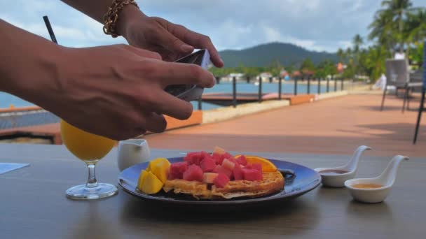 Жінка-блогер фотографує апельсиновий сік у кафе зі своїм телефоном. Молода жінка робить фото вафельки на смартфоні, фотографуючи їжу з мобільною камерою . — стокове відео