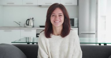 Parlak stüdyo ortamında gülümseyen güzel beyaz bir kızın portresi. Kanepede oturan kadın