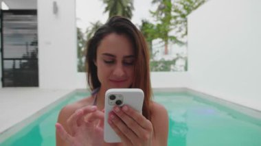 Ormanın arka planında havuzda otururken akıllı bir telefonla haberlere göz atmak.