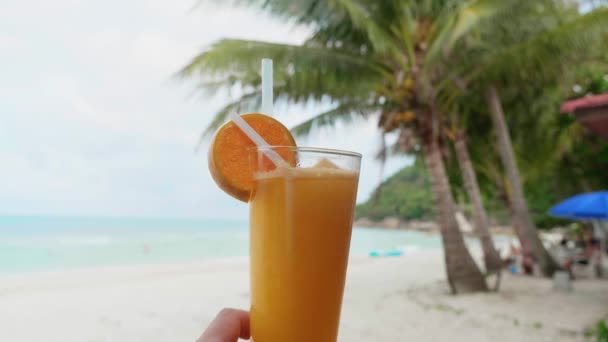 Mão segurando suco de laranja recentemente espremido com a linha do oceano e fundo da palma. — Vídeo de Stock