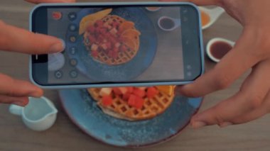 Akıllı telefonlu Top View yemek fotoğrafçılığı. Elleriyle Belçika Waffle 'larını tahta masa üzerinde karpuz parçalarıyla fotoğraflıyor. Yakın çekim..
