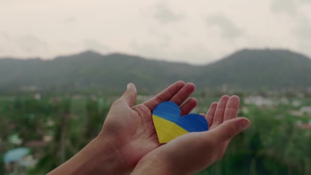 Primer plano retrato de la mano femenina sosteniendo la bandera de Ucrania en la forma de un corazón del fondo de la naturaleza. Proteger Ucrania — Vídeos de Stock