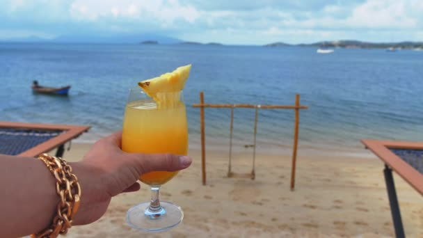 Самка держать в руке желтый ананас свежий, на берегу моря, летом волна волна для серфинга фон освежающий напиток расслабиться позитивный отдых настроение — стоковое видео