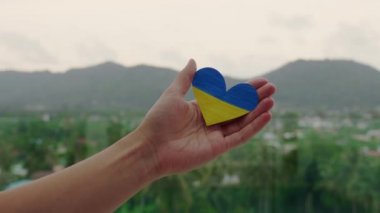 El, doğanın arka planında Ukrayna bayrağını kalp şeklinde tutuyor. Barış istiyoruz. Sivilleri koru.