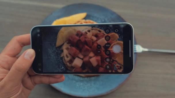 Donna sta mangiando waffle in caffè utilizza uno smartphone per scattare una foto. Vista dall'alto — Video Stock