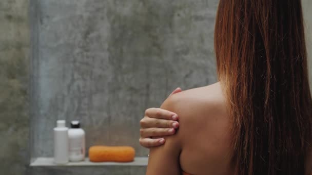 Primer plano del brazo femenino hidratando y masajeando su hombro sobre fondo azul, relajación y tratamiento de la piel después del baño — Vídeo de stock
