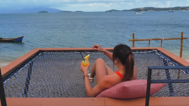 Woman Drinkig Fresh Smoothie on Beach in Hammock — Stock Video