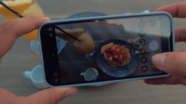 Akıllı telefonu kullanarak kırmızı meyveli ve mangolu waffle 'ın fotoğraflarını çeken kadın eller.