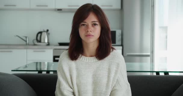 Een geschokte vrouw in trui en shirt die wow zegt en haar mond bedekt terwijl ze op de bank zit — Stockvideo