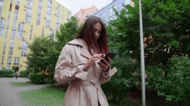Akıllı telefonu olan genç bir kadın sokakta yürüyor. Kamera hareket ediyor